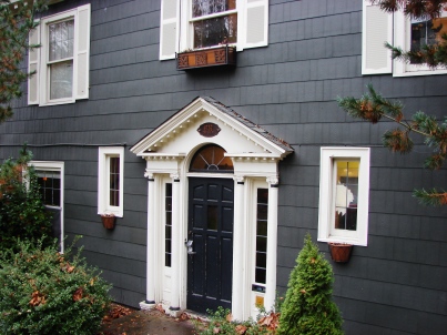 A Colonial house has an emphasized doorway with pillars and a triangular gable porch roof.  The doorway is usually centered and there is often symmetry in the placement of windows.